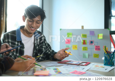Cheerful young man collaborating with his team on app design and UI UX development in the office Cheerful young man collaborating with his team on app design and UI UX development in the office 120976028