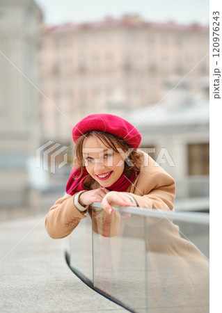 A young woman in a red beret smiles while leaning on a railing in an urban setting during daytime A young woman in a red beret smiles while leaning on a railing in an urban setting during daytime 120976243