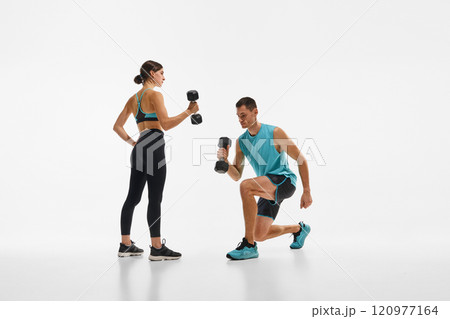 Muscular young man and fit young woman, couple in sportswear training together with dumbbells against white studio background 120977164
