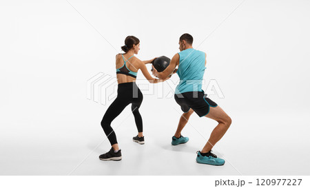 Sportive couple, young man and woman in sportswear training together, doing exercises with medicine ball against white studio background Sportive couple, young man and woman in sportswear training together, doing exercises with medicine ball against white studio background 120977227