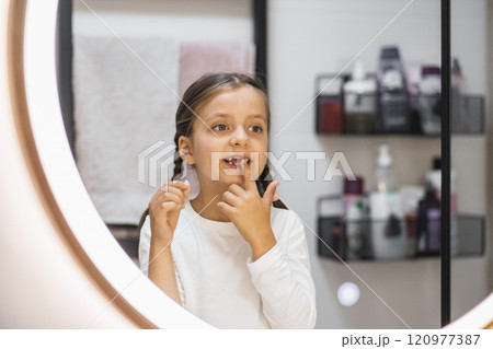 Portrait of young Caucasian girl examining lost tooth in bathroom mirror, showcasing childhood milestone. Expressive emotion captured in modern bathroom setting. 120977387