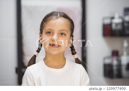 Caucasian girl with braided hair and missing teeth standing in bathroom. She is smiling at camera, conveying charm and innocence. Ideal for themes of childhood, growth, and family moments. 120977400