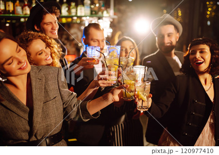 Cheering and drinking cocktails. Group of friends partying in nightclub, toasting drinks cocktails. 120977410