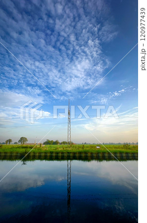 A serene landscape with a stunning reflection and an impressive tower under a cloudy sky A serene landscape with a stunning reflection and an impressive tower under a cloudy sky 120977439