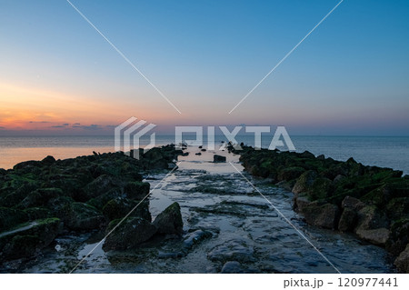 Experience the serene and breathtaking sunset occurring over the rocky jetty at dawn Experience the serene and breathtaking sunset occurring over the rocky jetty at dawn 120977441