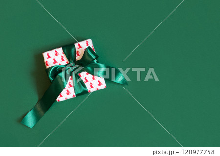 Christmas creative white gift box with green bow on green background. Xmas Holiday card. View from above. Copy space. Christmas creative white gift box with green bow on green background. Xmas Holiday card. View from above. Copy space. 120977758