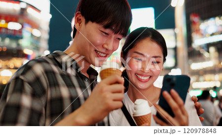 Happy couple, ice cream and phone for travel, date or check notification with bonding, love or contact in city. People, man and woman on smartphone, smile or gelato on social media at night in Japan Happy couple, ice cream and phone for travel, date or check notification with bonding, love or contact in city. People, man and woman on smartphone, smile or gelato on social media at night in Japan 120978848