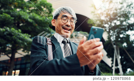 Outdoor, businessman and smile on smartphone on website for stock exchange rates in Japan. Mature person, city and happy as employee in finance on mobile app for market share or investment returns Outdoor, businessman and smile on smartphone on website for stock exchange rates in Japan. Mature person, city and happy as employee in finance on mobile app for market share or investment returns 120978868