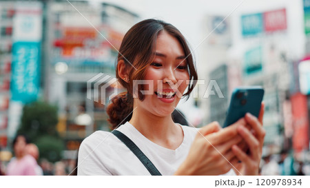 Woman, phone and happy with travel in city, reading and check notification with chat, laugh or meme in street. Girl, smartphone and outdoor on metro sidewalk, smile and app for social media in Japan Woman, phone and happy with travel in city, reading and check notification with chat, laugh or meme in street. Girl, smartphone and outdoor on metro sidewalk, smile and app for social media in Japan 120978934