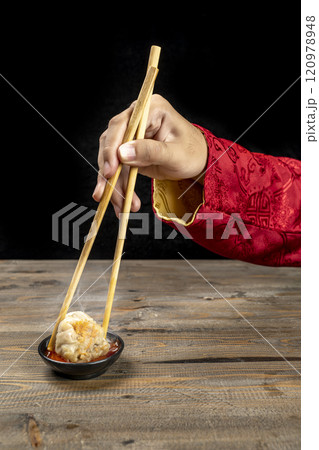 Chinese person with chopstick eating chinese dim sum dumpling with sauce 120978948