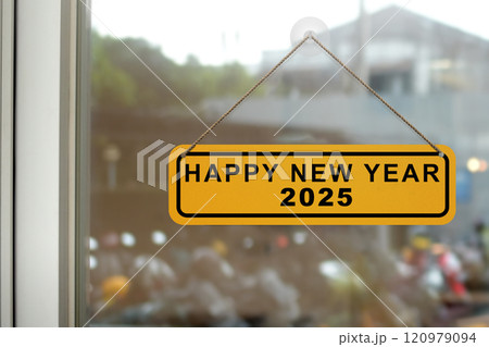 Hanging sign with text of Happy New Year 2025 on the window glass Hanging sign with text of Happy New Year 2025 on the window glass 120979094