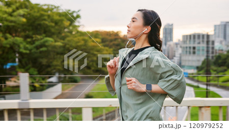 Japanese woman, running and earphones in city of sport exercise, marathon training and listen to music. Female athlete, cardio and workout practice of endurance performance, wellness and Japan bridge 120979252
