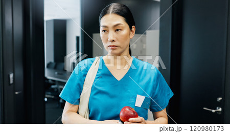 Thinking, nurse and Asian woman with apple in office for nutrition, healthcare or healthy food choice. Morning, breakfast ideas or surgeon in wellness clinic with fruit, fibre and vitamin c in Japan 120980173