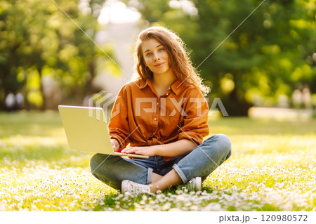 Young curly woman in the park on a green lawn with a laptop in her hands. Online education. Young curly woman in the park on a green lawn with a laptop in her hands. Online education. 120980572