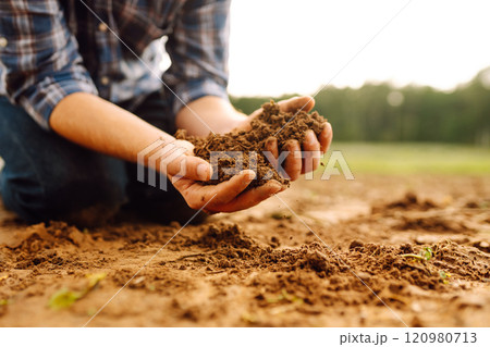 Soil is in the strong hands of a farmer on a black field. Agriculture or gardening concept. 120980713