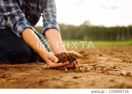 Soil is in the strong hands of a farmer on a black field. Agriculture or gardening concept. 120980716