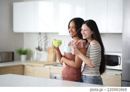 Happy interracial lesbian couple drinking affectionate in the kitchen 120981669