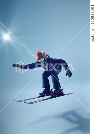 Skier leans into jump, her posture dynamic and expressive. Light blue backdrop enhances movement's fluidity. 120982301
