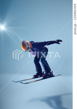 Athletic woman, skier ascends confidently holds poles trailing, illuminated by soft spotlight against blue gradient background. 120982304
