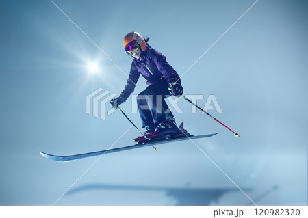 Winter athlete launching dynamically, orange helmet and reflective goggles glinting under studio lighting, emphasizing speed against seamless blue. Winter athlete launching dynamically, orange helmet and reflective goggles glinting under studio lighting, emphasizing speed against seamless blue. 120982320