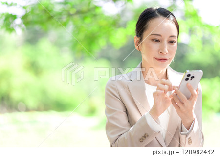 公園のベンチに座りながらスマートフォンを操作するビジネスウーマン 120982432