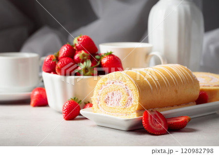 Delicious biscuit roll cake with fresh strawberries on a white stone table. 120982798