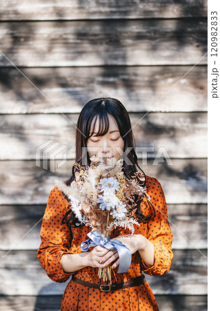 赤いワンピースを着て木漏れ日の中でドライフラワーを持って立っている女性 120982833