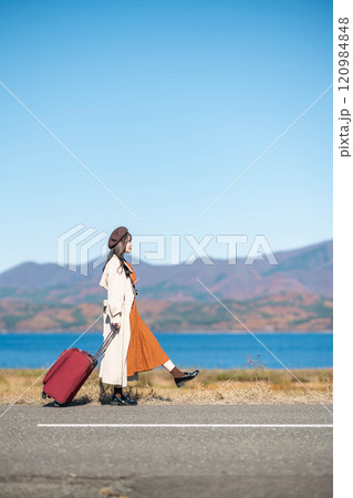 女子旅　キャリーバックを持って青空のもと歩いている若い女性 120984848