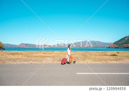 女子旅　キャリーバックを持って青空のもと歩いている若い女性 120984858