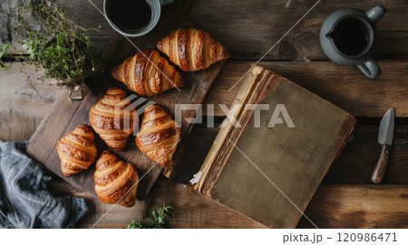 Freshly baked croissants on rustic kitchen counter with recipe book, coffee mugs, and herbs, creating warm and inviting atmosphere for baking enthusiasts 120986471