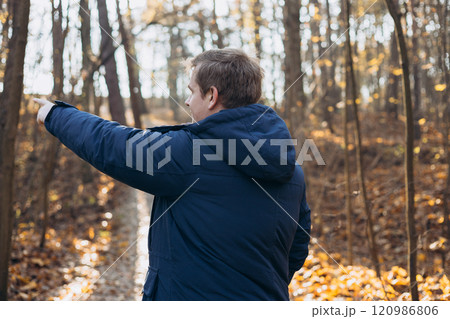 One Caucasian male hiking in the woods in autumn. Travel, active lifestyle, people and hobby concept. Blonde male in sport clothes pointing finger outdoors. Traveler enjoys eco-tourism, rear view One Caucasian male hiking in the woods in autumn. Travel, active lifestyle, people and hobby concept. Blonde male in sport clothes pointing finger outdoors. Traveler enjoys eco-tourism, rear view 120986806