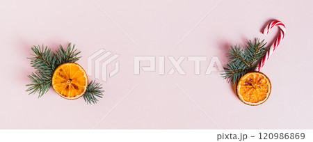 Christmas arrangement of fir branches, dried orange and candy cane on pink top view web banner 120986869