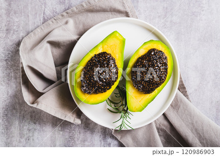 Close up of black chia caviar in avocado halves on a plate on the table top view 120986903