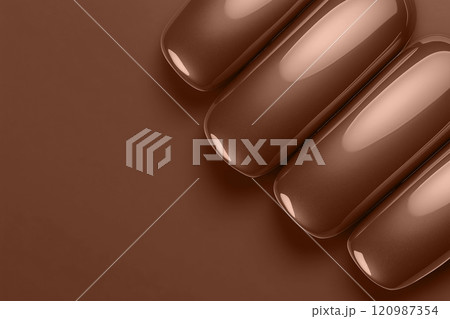 Closeup of metallic mocha mousse brown nails against a matte chocolate backdrop. Modern trendy tone hue shade 120987354