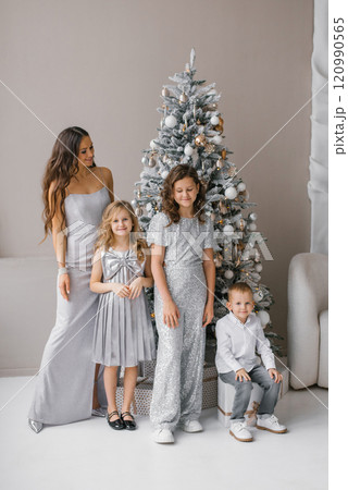 Happy family of four posing in front of Christmas tree. Mother is wearing long dress and the children are wearing sparkly outfits 120990565