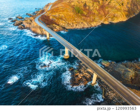 Aerial view of bridge, blue ocean and rocky coastline at sunset 120993563
