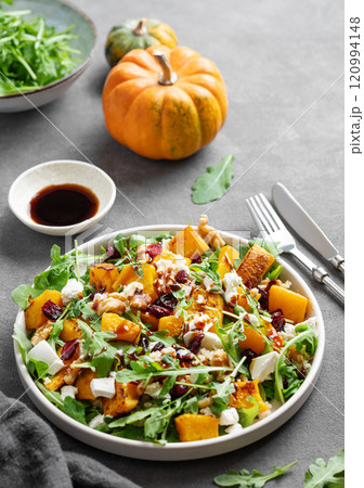Salad with pumpkin, arugula, feta cheese, nuts and dried berries in a plate on dark background 120994148