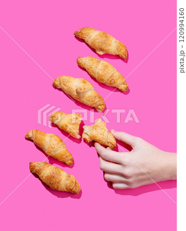Hand holding fresh torn mini croissant on pink background with shadow. Design flat lay concept 120994160