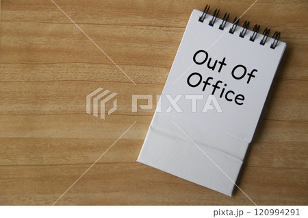 Top view of Out Of Office text on white notepad on wooden desk. Away from work concept 120994291