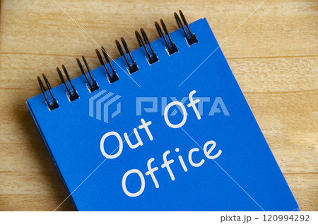 Top view of Out Of Office text on blue notepad on wooden desk. Away from work concept Top view of Out Of Office text on blue notepad on wooden desk. Away from work concept 120994292