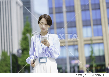 オフィス街でノートパソコンを手にスマホで会話するビジネスウーマンのポートレート 120996510