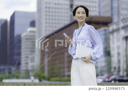 オフィス街でノートパソコンとスマホを持つビジネスウーマンのポートレート オフィス街でノートパソコンとスマホを持つビジネスウーマンのポートレート 120996573