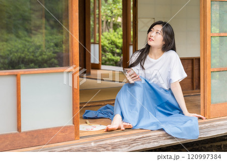 古民家の縁側でスマホを眺めてる若い女性　ネットショッピング- 120997384