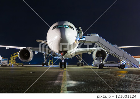Front view of white wide-body passenger airplane with a boarding steps at the night airport apron 121001124
