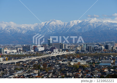 2024.12北陸新幹線と富山市中心部のビル街と冠雪の北アルプス剱岳立山連峰 121002221