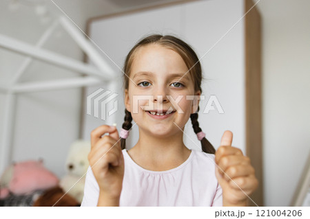 Happy Caucasian girl with braided hair showing fallen baby tooth in cozy home setting, expressing excitement. Happy Caucasian girl with braided hair showing fallen baby tooth in cozy home setting, expressing excitement. 121004206