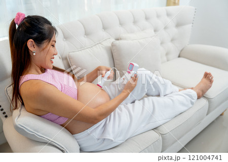 Back of Asian pregnant woman lie on sofa and use tools for listen sound in her belly and look happy at home. Back of Asian pregnant woman lie on sofa and use tools for listen sound in her belly and look happy at home. 121004741