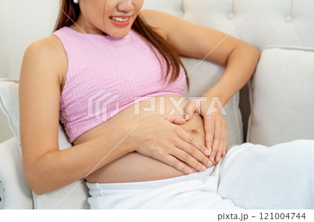 Side view and close up pregnant woman sit on sofa and put hands on her belly with heart shape. Side view and close up pregnant woman sit on sofa and put hands on her belly with heart shape. 121004744