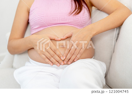 Close up pregnant woman sit on sofa and put hands on her belly with heart shape. Close up pregnant woman sit on sofa and put hands on her belly with heart shape. 121004745