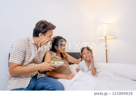 Wide shot Asian father hold dish of food and give to little girl with pregnant mother stay on bed in concept of happiness family in their house. 121004819